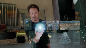 The character Tony Stark from the Avengers movie holds a 3d hologram cube surrounded by other holographic displays