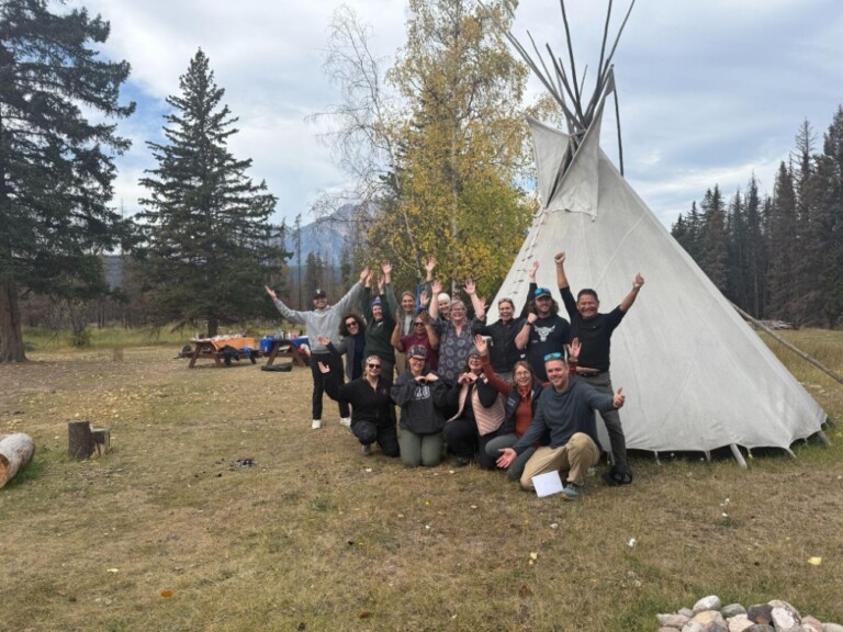 Several happy and joyous people from the GO-GN Canada Hub are pictured in front of a tipi.